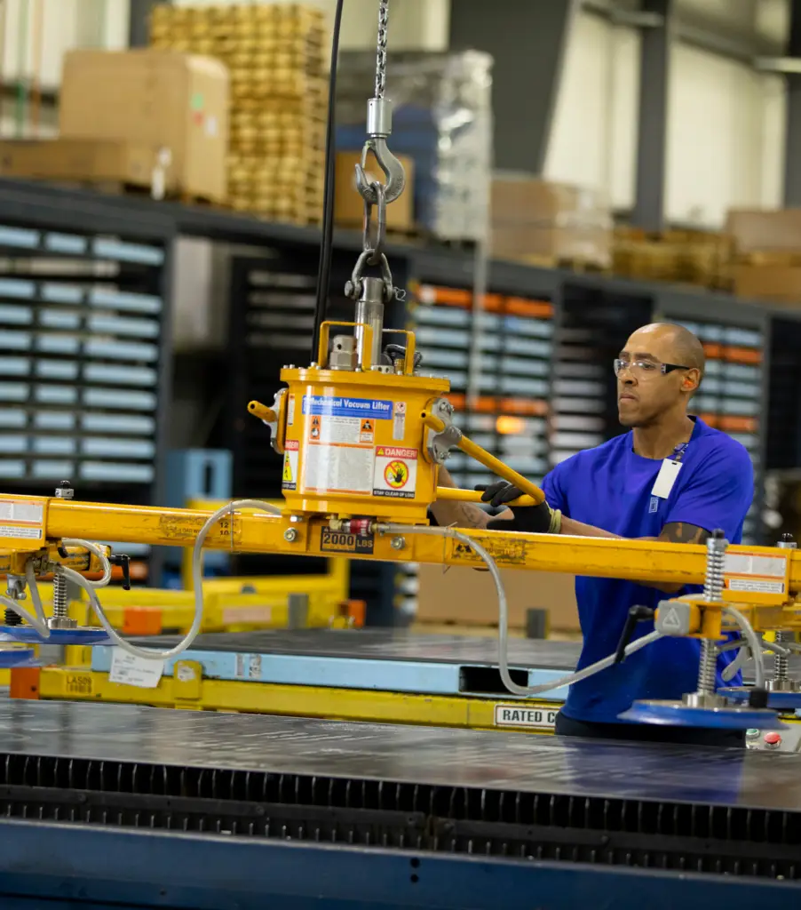 GSM technician loading sheet metal onto laser cutting table at manufacturing facility